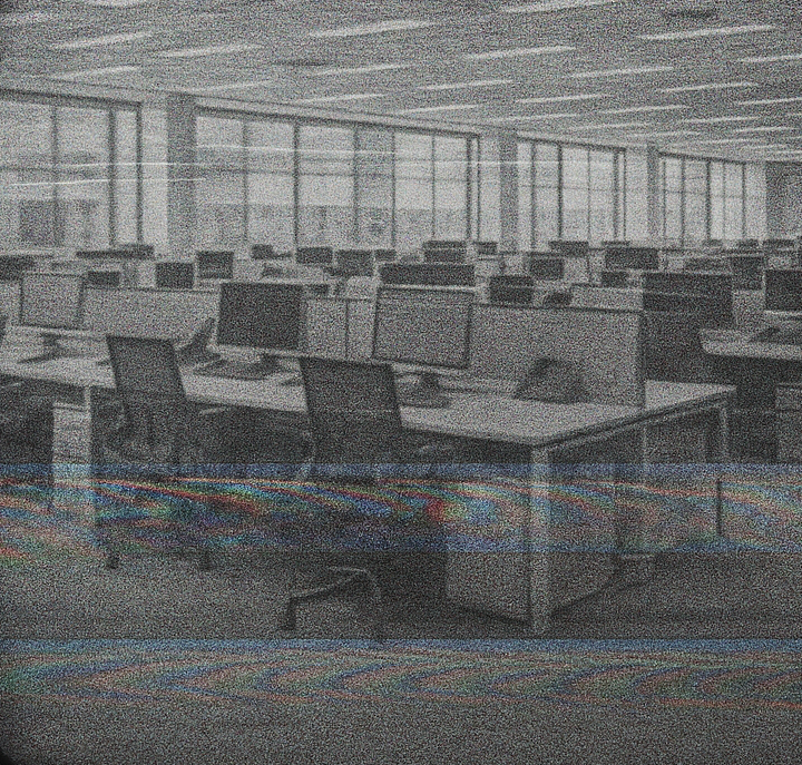 a flickering TV screen displays an empty open plan office with rows and rows of desks and computer stations