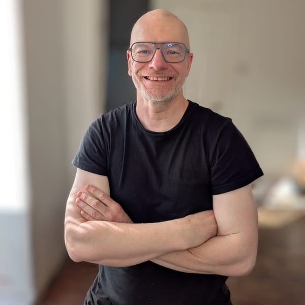Portrait photo of the author. Si is smiling, with his arms crossed. He's wearing a black t-shirt.